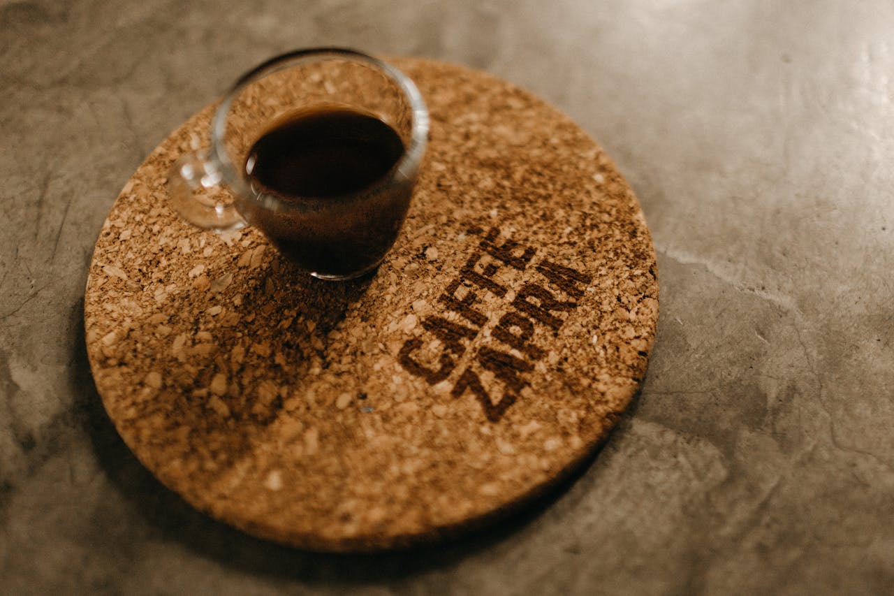 services-01 A cork coaster holding a glass of black coffee on a concrete surface.